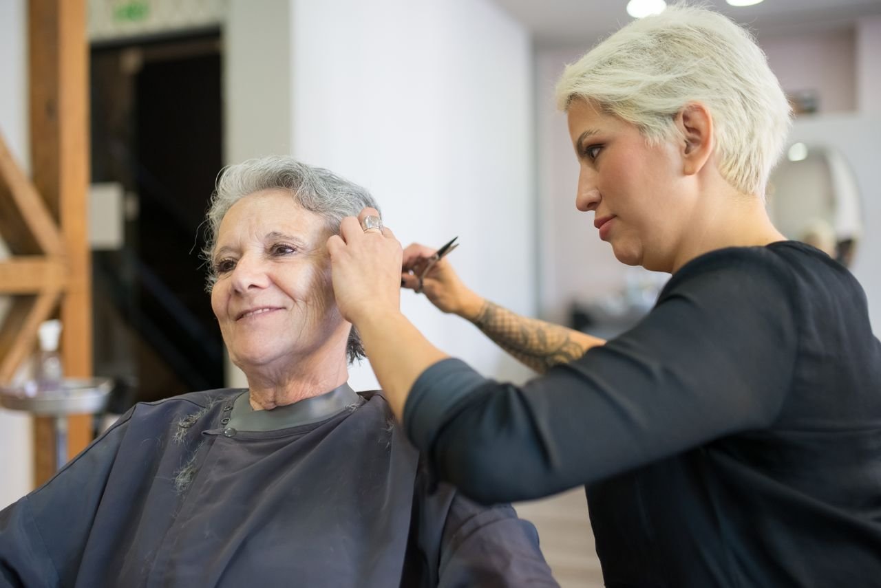 A hairstylist giving a haircut to a senior woman in a well-lit salon setting in Portugal.